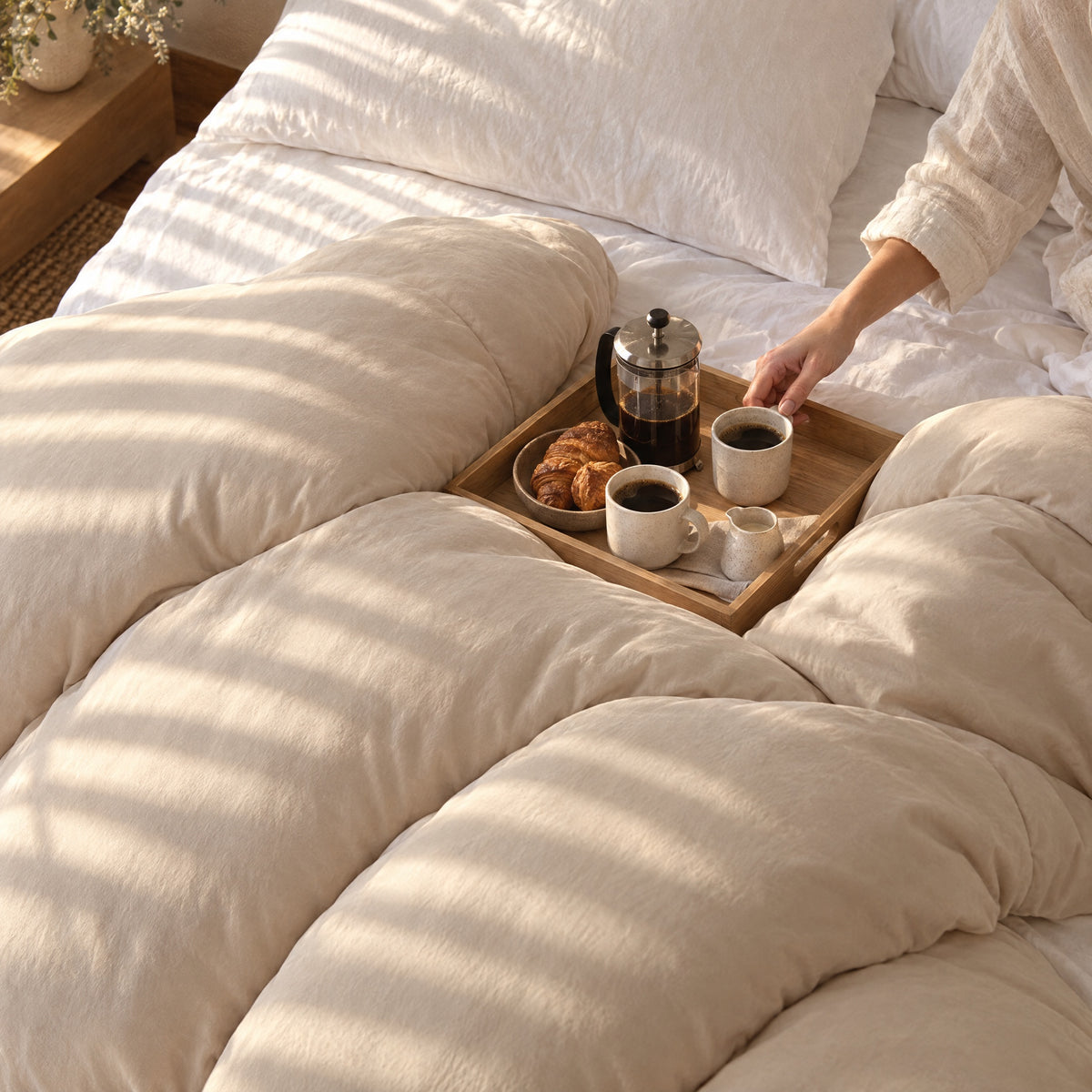 Unmade bed with the Nimbus Comforter in Sand and a breakfast tray