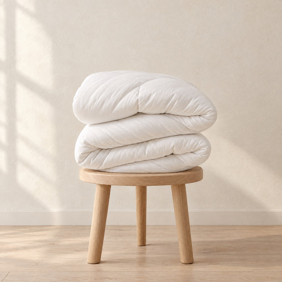 Nimbus Comforter in White folded on an oak stool